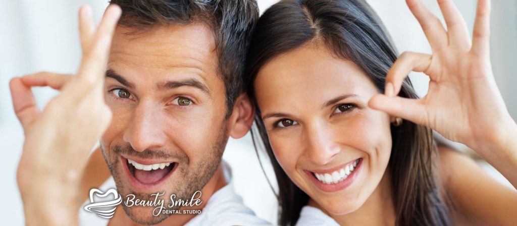 Una pareja sonriente haciendo un pulgar hacia arriba frente a una clínica dental moderna, satisfecha con sus servicios dentales en Tijuana.